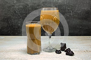 Fruit smoothie in a glass on a table decorated with prunes. Side view.