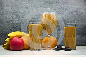 Fruit smoothie in glasses, with fruits on the table.