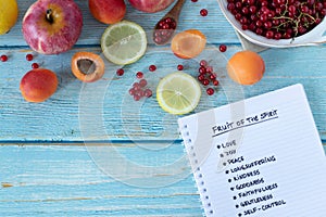 Fruit of the Spirit handwritten words in notebook from Galatians Bible Book on wooden table with fresh colorful fruit, top view