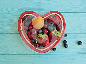 fruit strawberry, blueberry, cherry, apricot detox plate heart on blue wooden