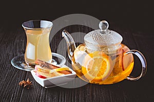 Fruit tea in glass teapot and cup on black background