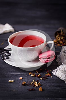 Fruit tea and pink raspberry macaron on black wooden background. Traditional French sweets