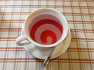 Fruit tea in a white cup on a table covered with a checkered tablecloth