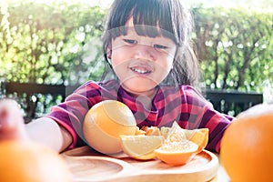 Fruit and Vegetable for Kids Concept. Little Cute 3-4 Years Old Girl with Sliced Orange on Wooden Plate. Fresh Juicy Fruit in