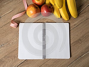 Fruits apple and bananas, blank notebook and centimeter on wooden table, top view, flatlay