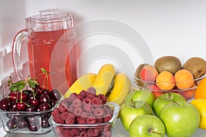Fruits, berries and a drink lie inside a white open refrigerator, close-up