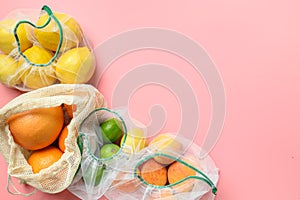 Fruits and citrics in reusable eco-friendly mesh bags on pink background. Zero waste shopping.