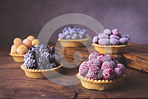 Fruits with hoarfrost in tartlets on a dark old wooden background.