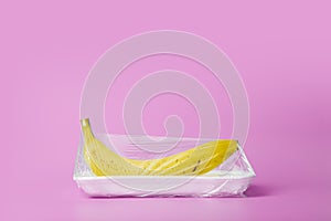 Fruits in plastic packaging from the supermarket are minimal. Banana in cellophane and non-degradable plastic on a blue