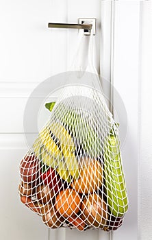 Fruits and vegetables hang on the handle of a white door in a string bag. onions zucchini bananas pepper orange. eco zero waste