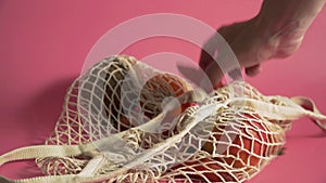 Fruits and vegetables in mesh bag, alternative to plastic shopping bags on pink background 4k