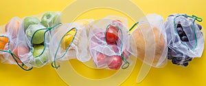 Fruits and vegetables in reusable eco-friendly mesh bags on bright yellow background. Zero waste shopping. Ecological concept.