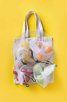 Fruits and vegetables in reusable eco-friendly mesh bags on bright yellow background. Zero waste shopping. Ecological concept.