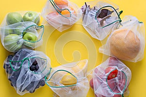 Fruits and vegetables in reusable eco-friendly mesh bags on yellow background. Zero waste shopping. Ecological concept. Stop