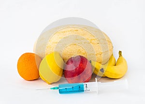 Fruits on a white background bananas, orange, melon, lemon and nectarine, next is a syringe with gmo and nitrates, genetically