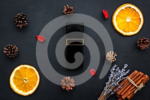 Fruity and pine perfume for women. Bottle of perfume near orange, lavender, cinnamon, pine cones on black background top