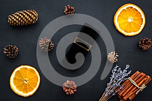 Fruity and pine perfume for women. Bottle of perfume near orange, lavender, cinnamon, pine cones on black background top