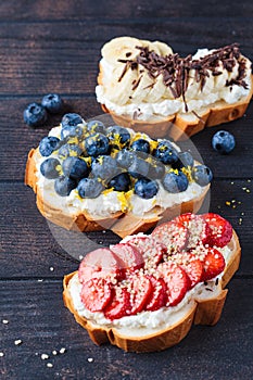 Fruity vegetarian toasts for breakfast on dark background. Bread slices with ricotta, berries, banana, chocolate and seeds