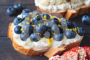 Fruity vegetarian toasts for breakfast on dark background. Bread slices with ricotta, berries, banana, chocolate and seeds