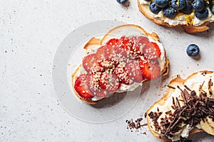 Fruity vegetarian toasts for breakfast on gray background. Bread slices with ricotta, berries, banana, chocolate and seeds
