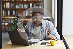 Frustrated African American man with laptop studying or working in coffee shop