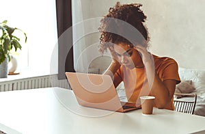 Frustrated African descent young woman in front of laptop at home, receiving e-mail with bad news