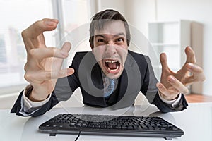 Frustrated angry businessman is shouting and working with computer in office