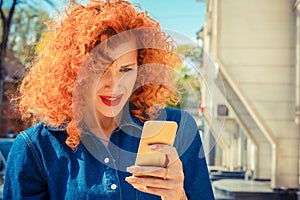 Frustrated angry woman with red curly hair looking to mobile phone