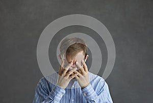 Frustrated ashamed desperate man hiding his face in his hands on grey studio background