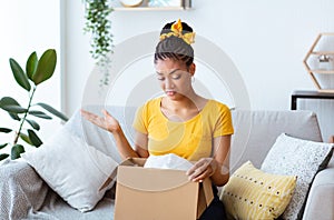Frustrated black woman unpacking wrong box, delivery mistake