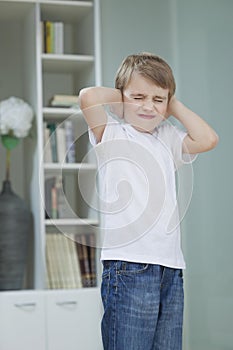 Frustrated boy covering his ears with hands at home