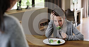 Frustrated boy told to eat healthy vegetables that he hates eating by his mom at meal time on his dinner plate. Mother