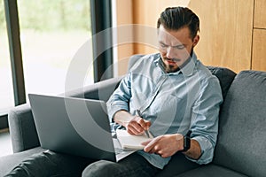 Frustrated brunette man freelancer working with laptop and making notes