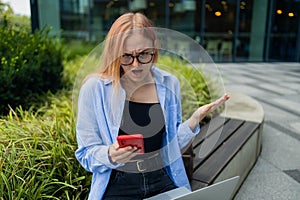 Frustrated business woman received bad news in e-mail on mobile phone while sits outside company near copy space