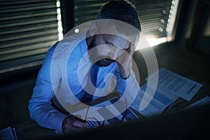 Frustrated businessman with computer sitting at desk, working late. Financial crisis concept.