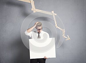 Frustrated businessman holding panel in front of graph pointing