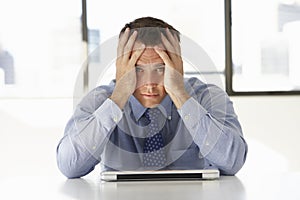 Frustrated Businessman Sitting At Desk In Office Using Laptop