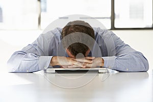 Frustrated Businessman Sitting At Desk In Office Using Laptop