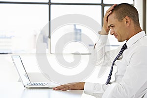 Frustrated Businessman Sitting At Desk In Office Using Laptop