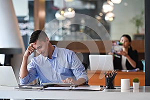 Frustrated businessman sitting in front of laptop computer at office desk.