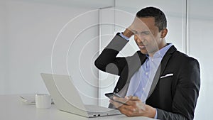 Frustrated casual afro-american businessman reacting to loss while using smartphone