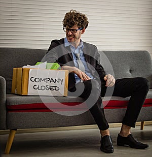 Frustrated Caucasian businessman sitting on a couch looking at a box of his belongings. Feeling discouraged and hopeless.