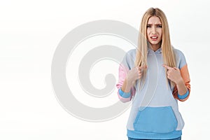 Frustrated and confused blonde glamour girl with blonde hair, looking offended or accused, pointing at herself and