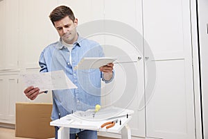 Frustrated And Confused Man Reading Instructions And Putting Together Self Assembly Furniture At Home