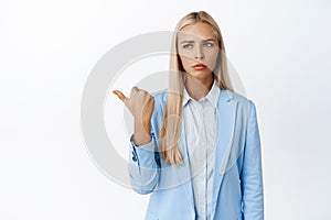 Frustrated corporate woman, pointing finger left and looking disappointed at advertisement, standing over white