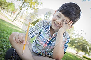 Frustrated Cute Young Boy Holding Pencil Sitting on the Grass