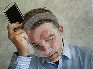 Frustrated and depressed business man holding mobile phone in stress feeling disappointed suffering headache and anxiety looking