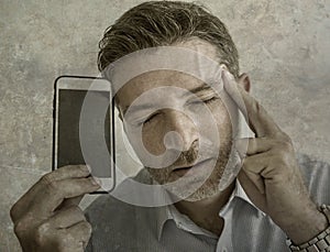 Frustrated and depressed business man holding mobile phone in stress feeling disappointed suffering headache and anxiety looking