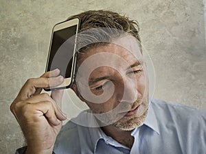 Frustrated and depressed business man holding mobile phone in stress feeling disappointed suffering headache and anxiety looking