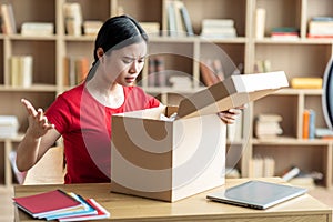 Frustrated disappointed young japanese lady opens cardboard box and sad for mistake with parcel